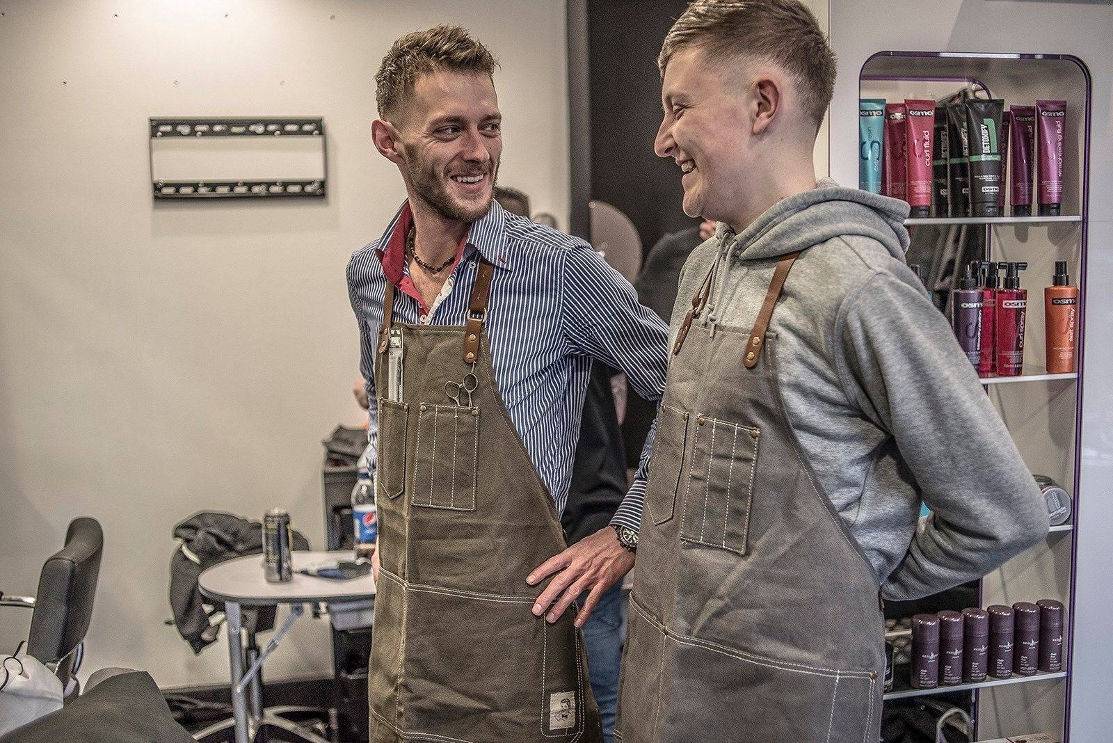 Two of the barbers in aprons by the product shelves